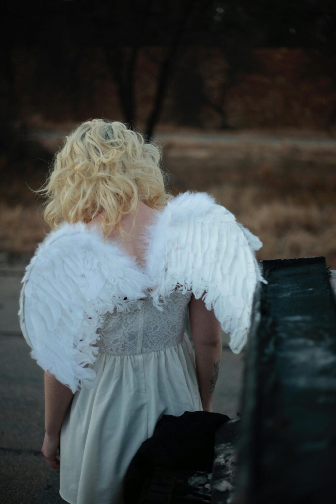 Woman with angel wings standing outdoors in a creative fashion ensemble, seen from behind.